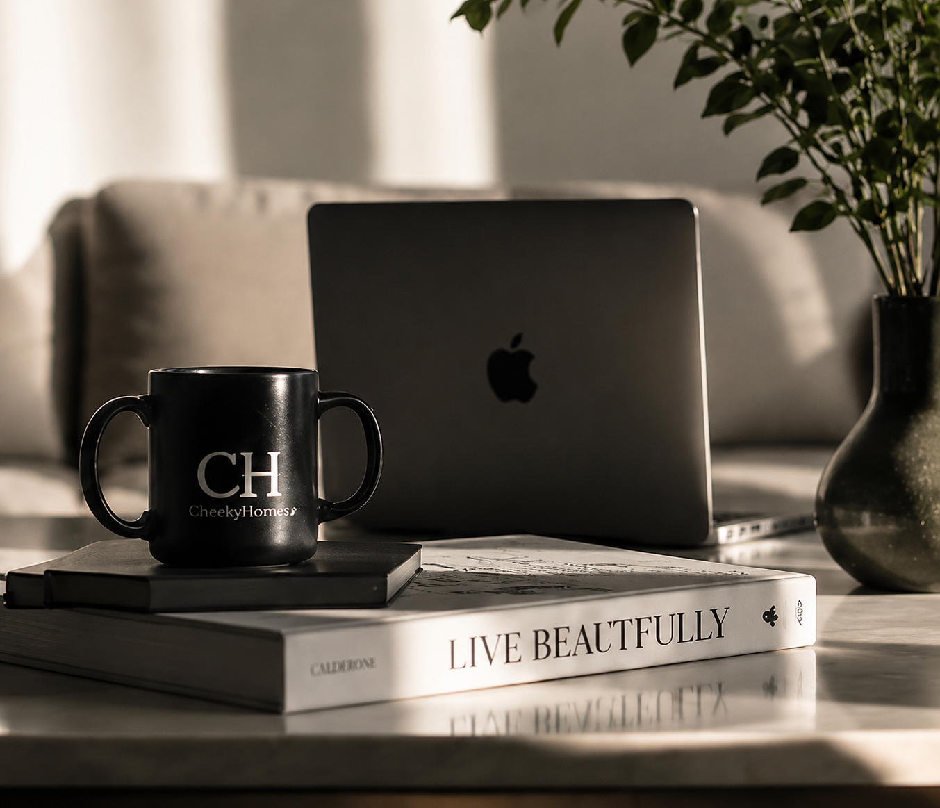 CheekyHomes branded mug beside a laptop and styling books